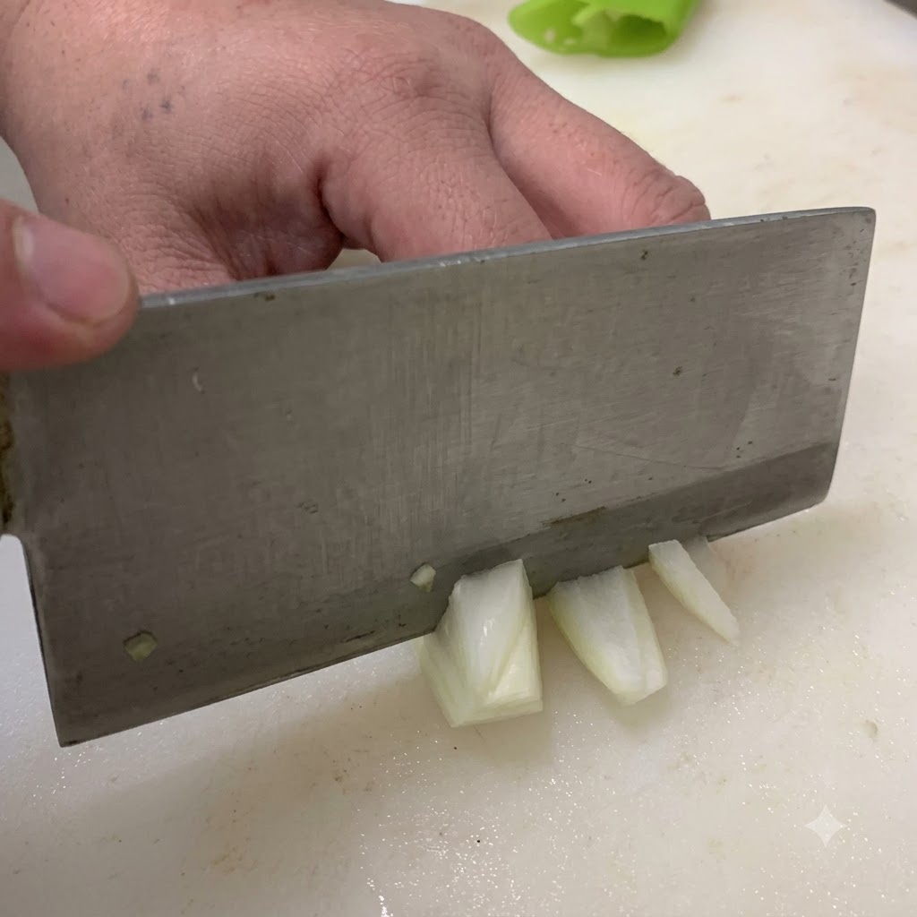 Un coltello che taglia una cipolla a pezzi su un tagliere bianco.