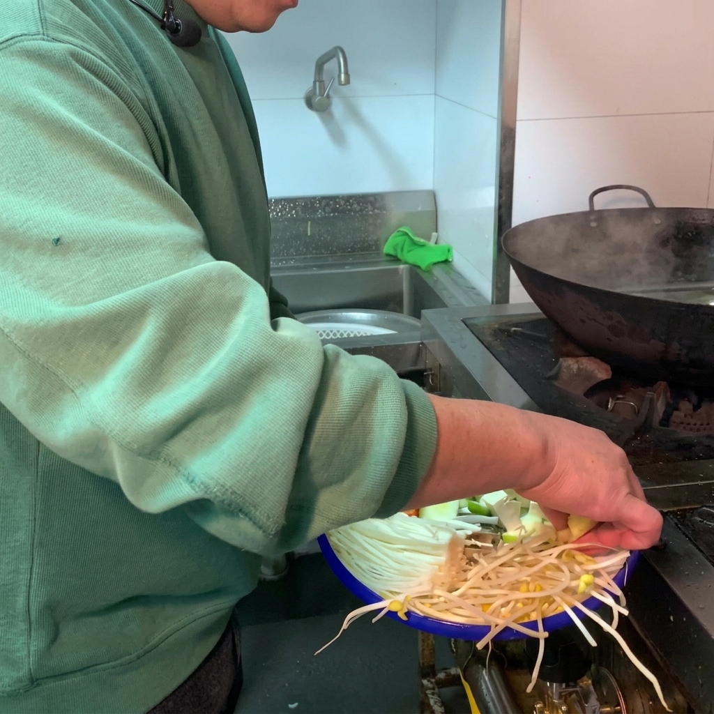 Una varietà di verdure fresche e tofu bianco aggiunti in una pentola di terracotta scura riempita dacqua.