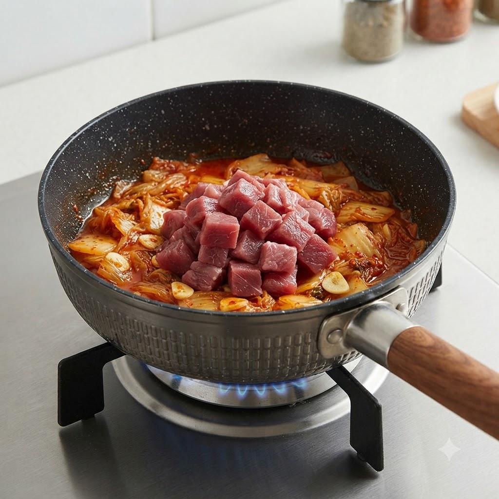 Cubetti di manzo crudo posizionati sopra il kimchi saltato in una pentola.