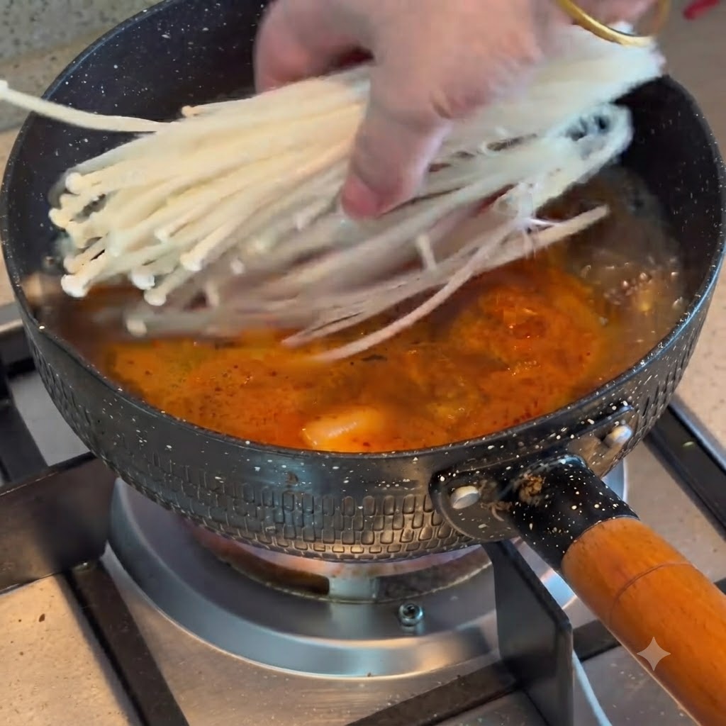 Funghi enoki aggiunti in una pentola di stufato di kimchi e manzo in ebollizione.