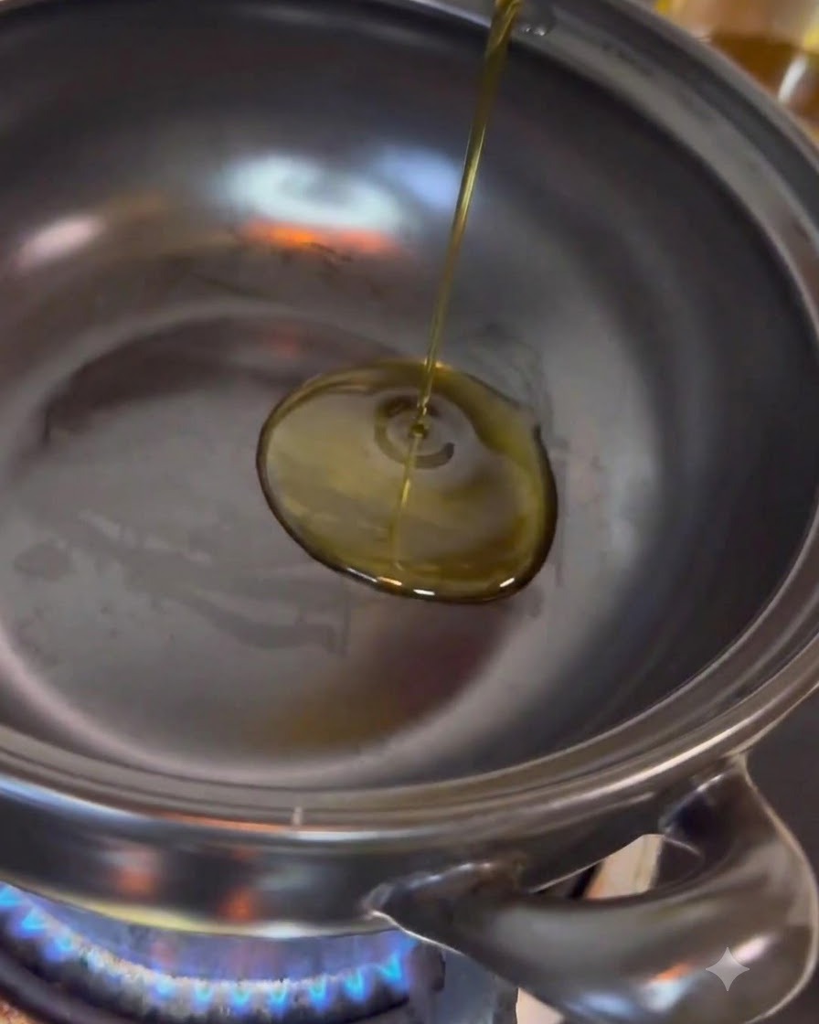 Olio da cucina trasparente versato al centro di una pentola in acciaio inossidabile posizionata su una fiamma blu attiva.