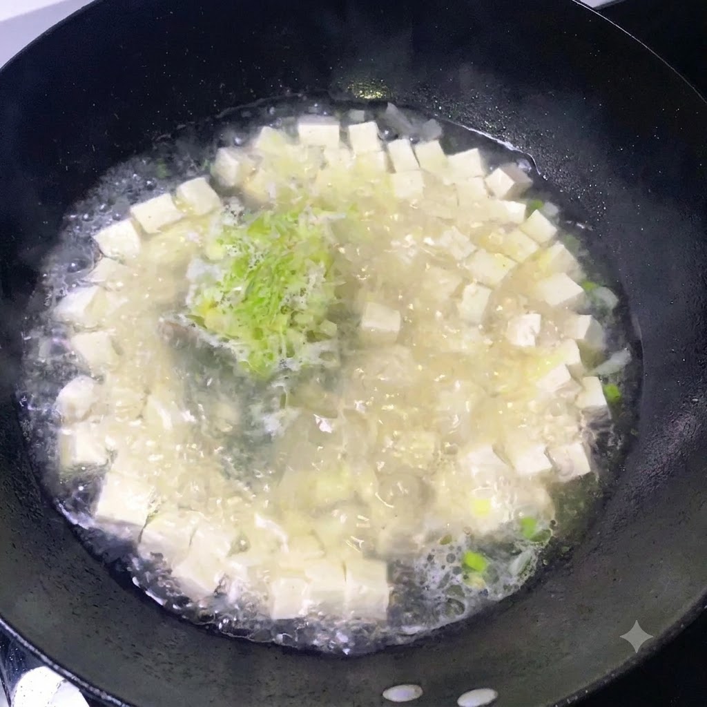 Condimenti cosparsi su una pentola ribollente di zuppa di tofu e cipolle verdi tritate.