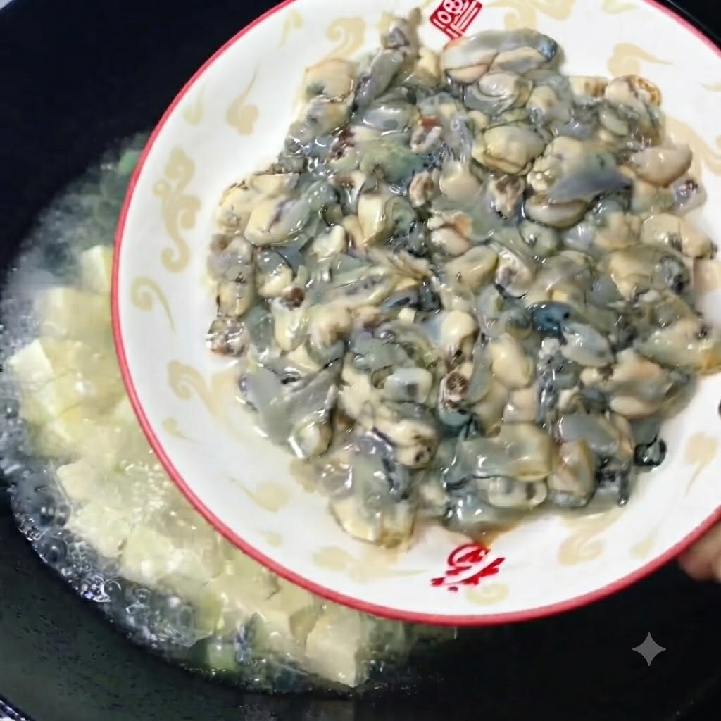Ostriche crude fresche e polpose fatte scivolare da un piatto decorativo in un wok di brodo di tofu in ebollizione.