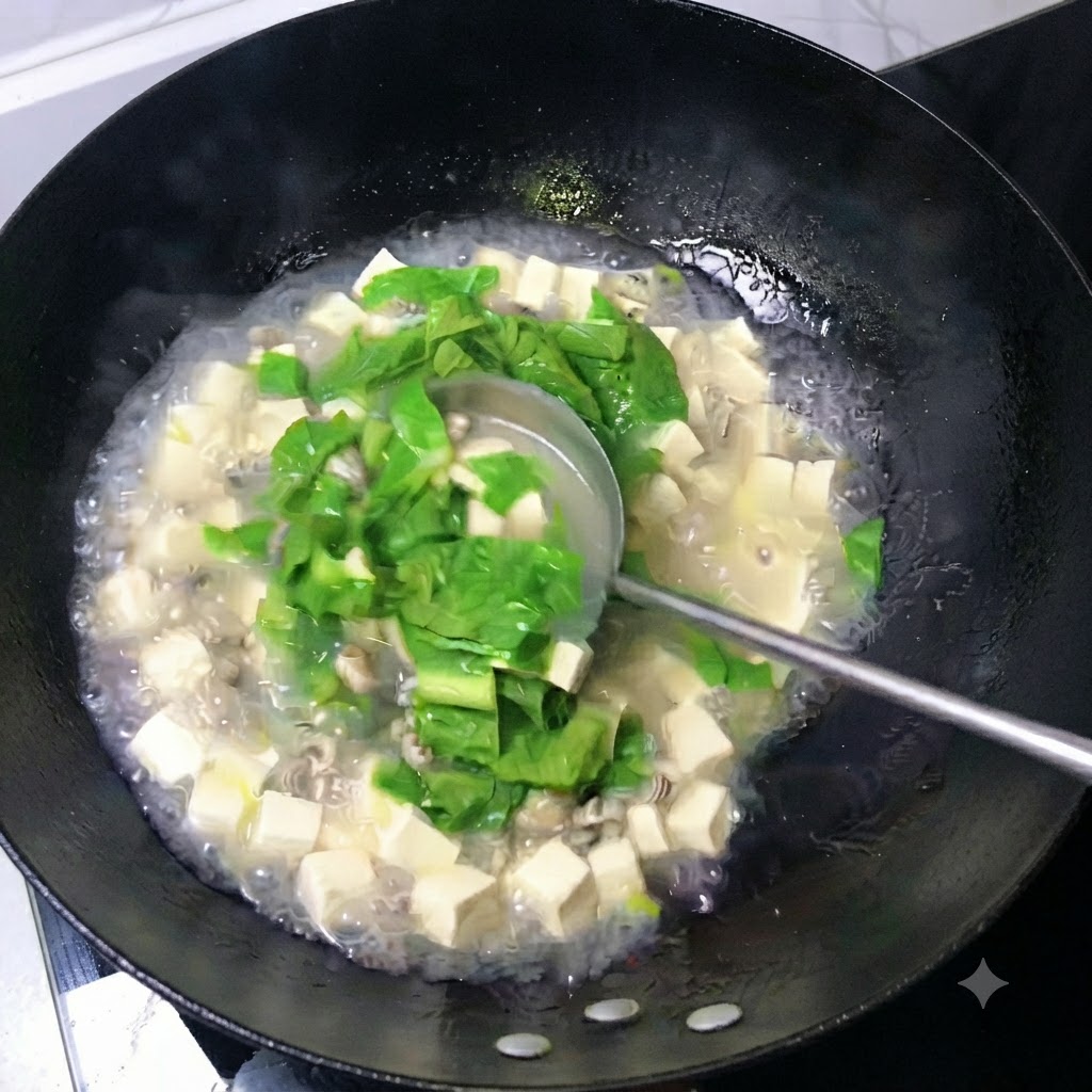 Un mestolo che mescola un brodo bianco latte pieno di cubetti di tofu, ostriche e foglie verdi in un wok.