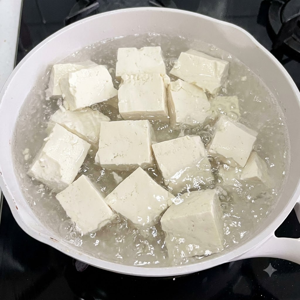 Cubetti di tofu in ebollizione in una pentola bianca con fettine di zenzero.