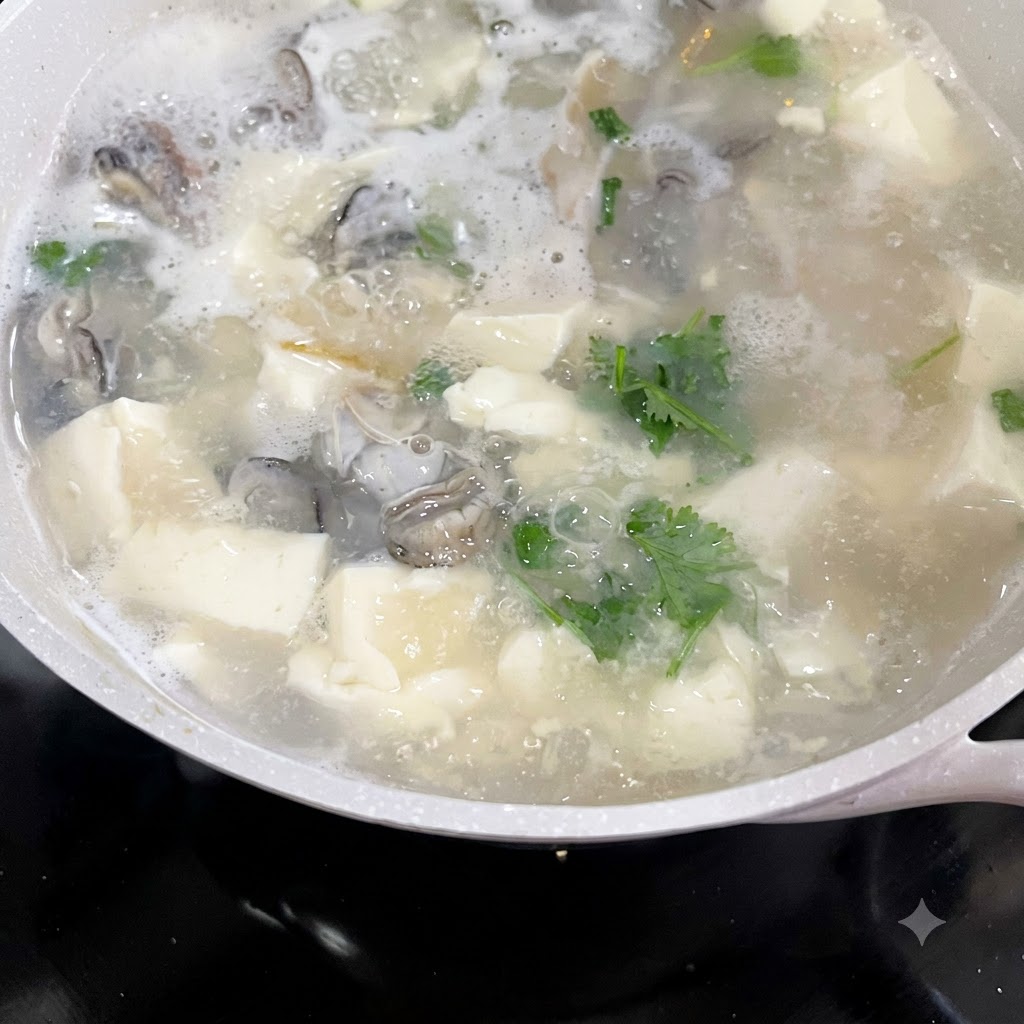 Coriandolo tritato e cipollotti aggiunti a una pentola ribollente di zuppa di ostriche e tofu.