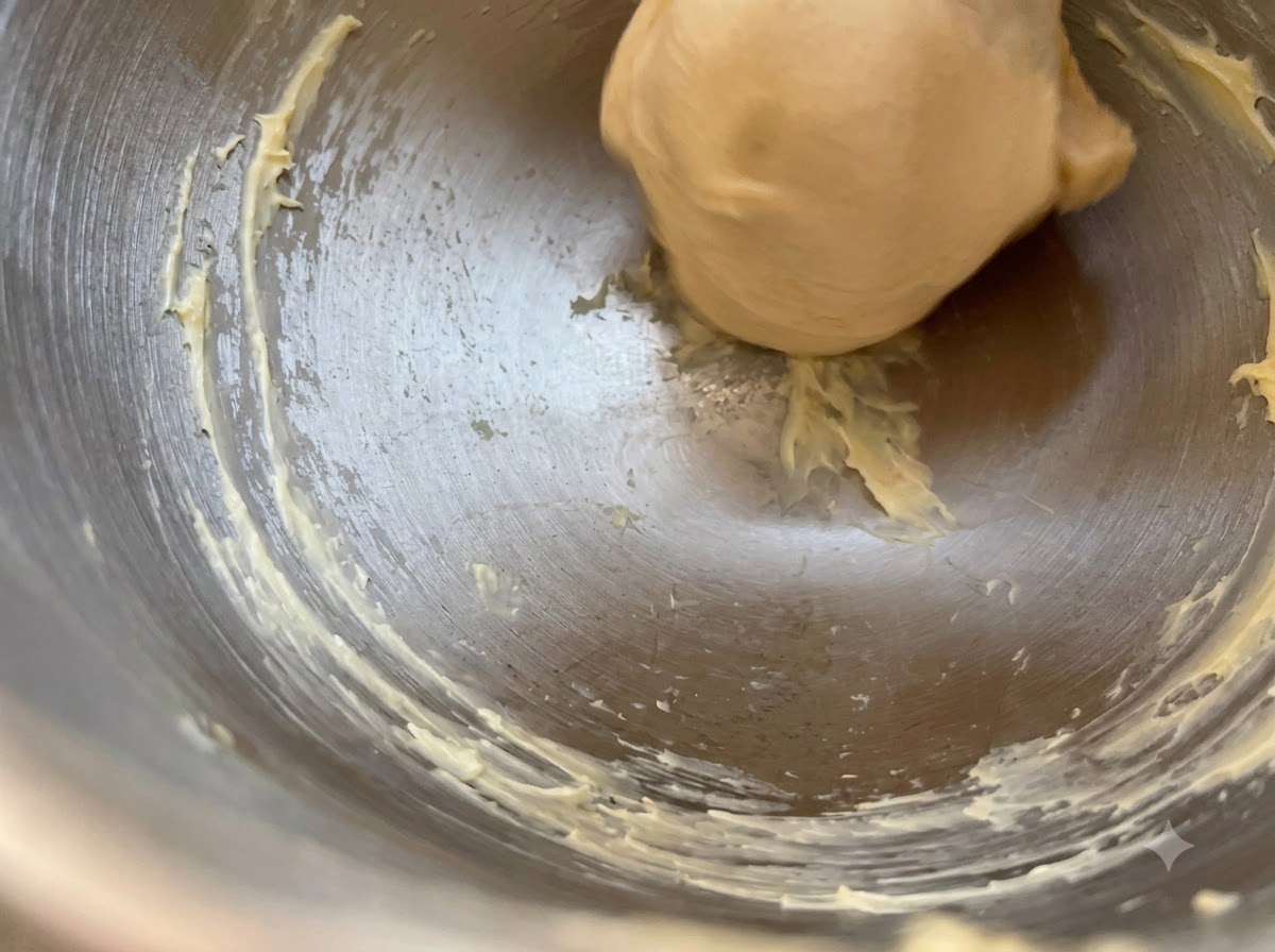 Una palla liscia di pasta lievitata che riposa allinterno di una ciotola di metallo con strisce di burro lungo i bordi.