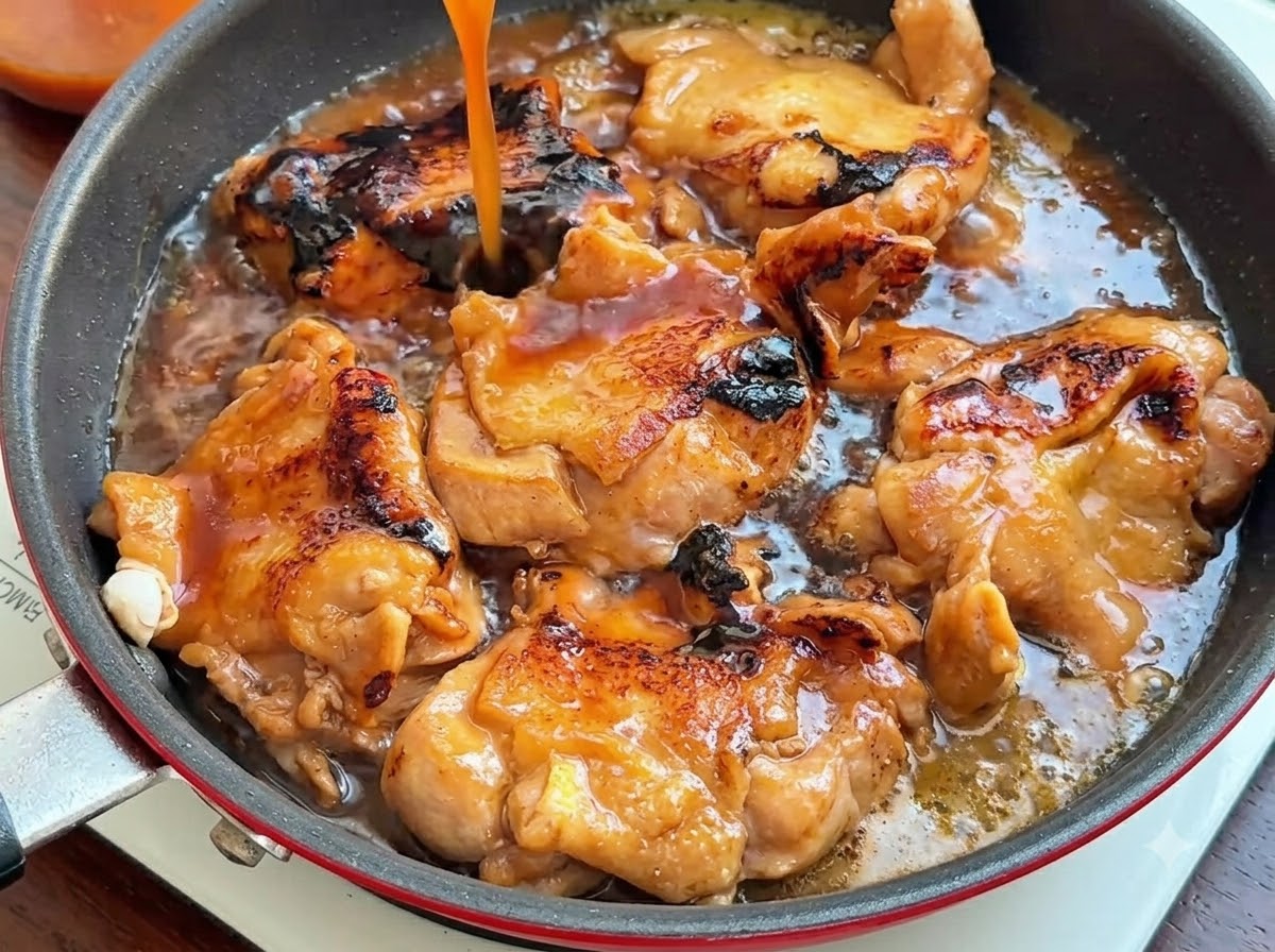 Un flusso di salsa marrone scuro che viene versato dallalto in una padella piena di cosce di pollo rosolate.