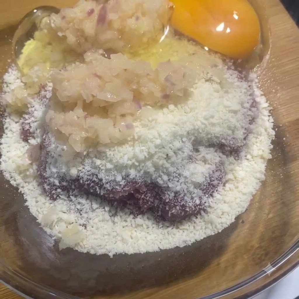 Un tuorlo e un albume crudi in una ciotola di vetro insieme alla miscela di carne e cipolla.