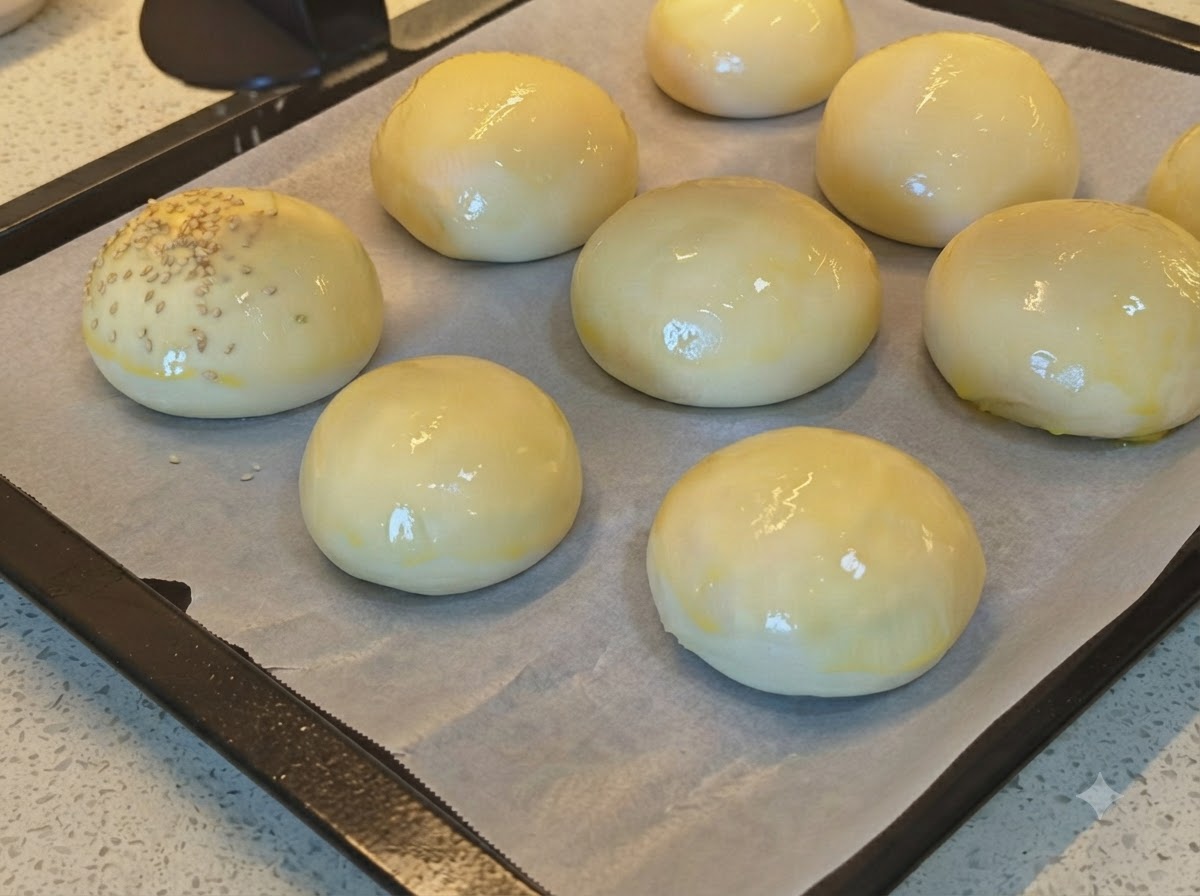 Semi di sesamo sparsi su una teglia di panini per hamburger lucidi e spennellati con luovo.