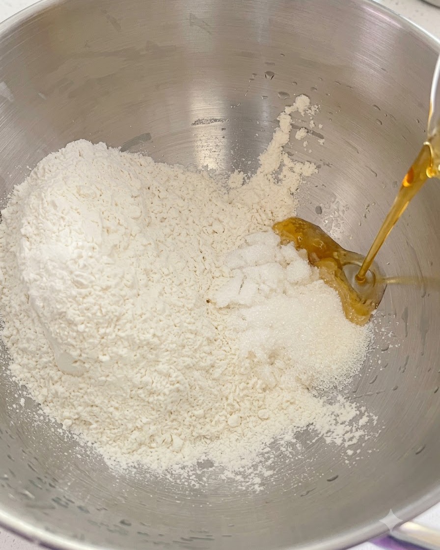 Farina secca, zucchero e ingredienti liquidi versati insieme allinterno di una ciotola di una planetaria in metallo.