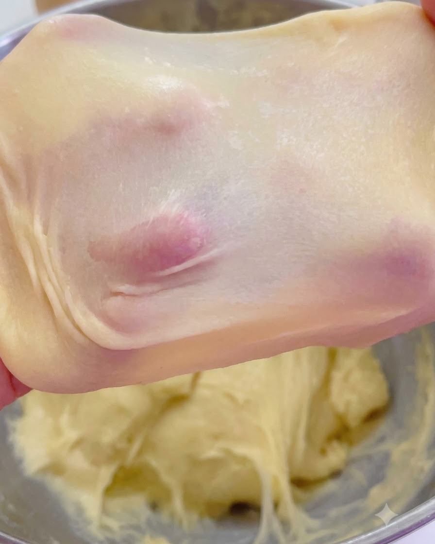 Impasto brioche allungato che mostra una membrana a finestra sottile e traslucida trattenuta dalle dita.
