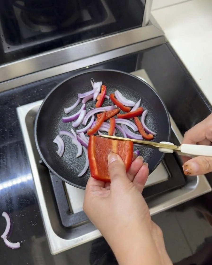 Cipolle rosse e peperoni affettati in una padella conditi con sale e pepe usando le forbici da cucina.