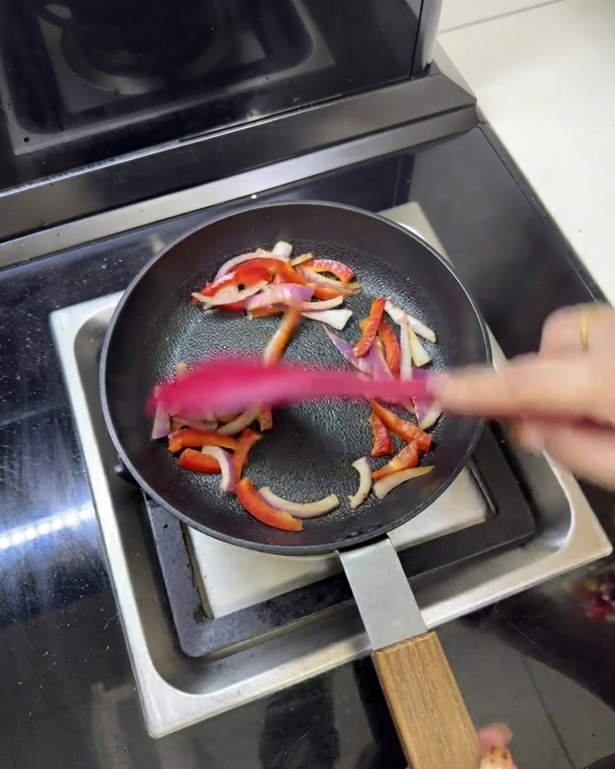 Strisce di carne precotta saltate insieme a cipolle rosse e peperoni in una padella.