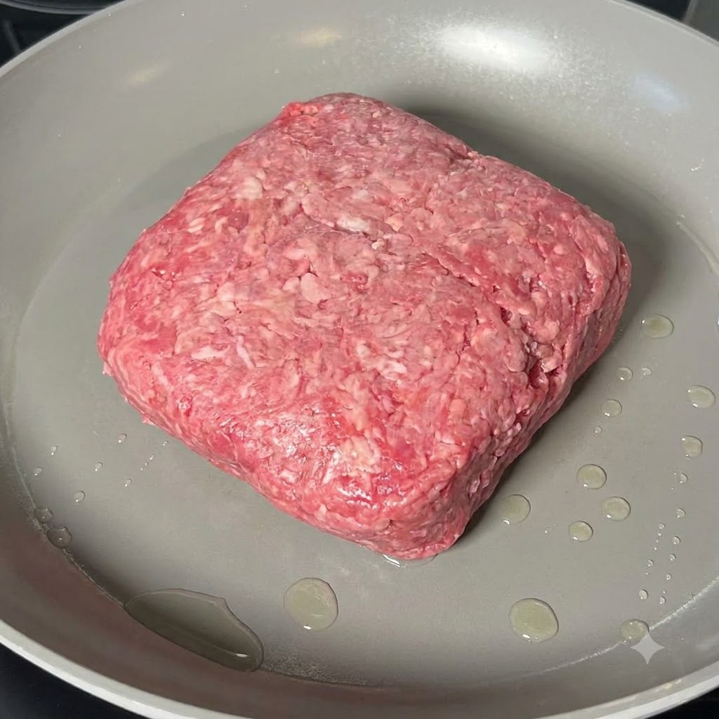Carne macinata in cottura sminuzzata con una spatola di legno in una padella capiente.