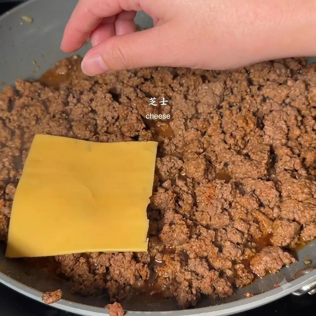 Una fetta di formaggio quadrata gialla posizionata sopra la carne macinata cotta in padella da una mano.