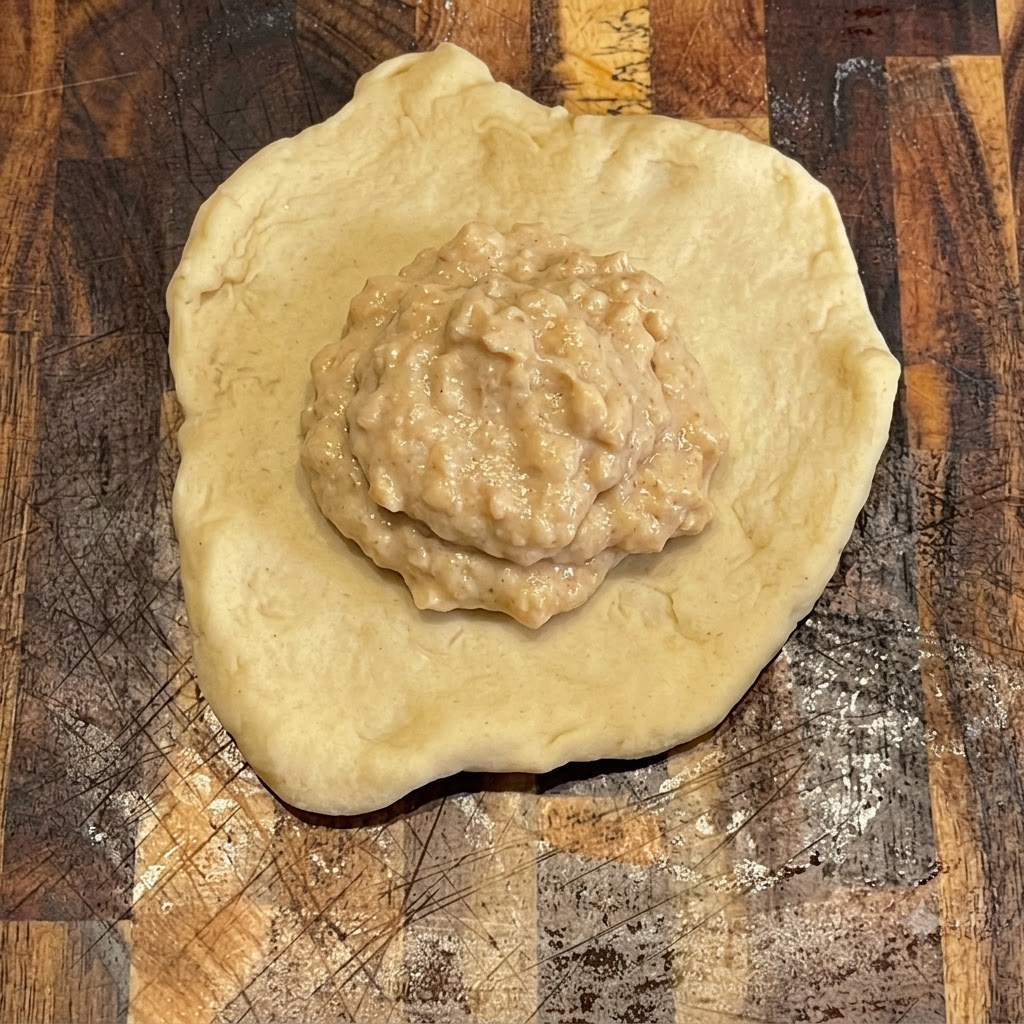 Salsa per hamburger spalmata ordinatamente sopra un pezzo di impasto rotondo e piatto su un tagliere di legno.