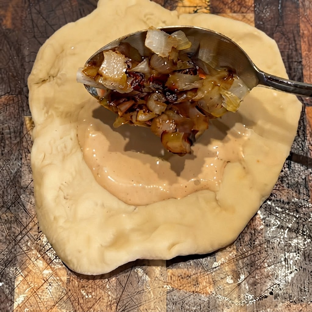 Cipolle grigliate messe con un cucchiaio sopra lo strato di salsa sullimpasto.