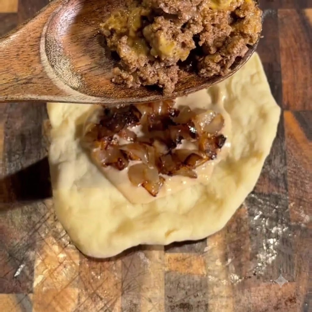 Carne macinata cotta aggiunta con un cucchiaio di legno sopra le cipolle e la salsa.