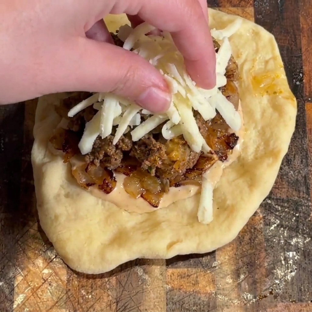 Formaggio mozzarella grattugiato spolverato sopra il ripieno del burger.