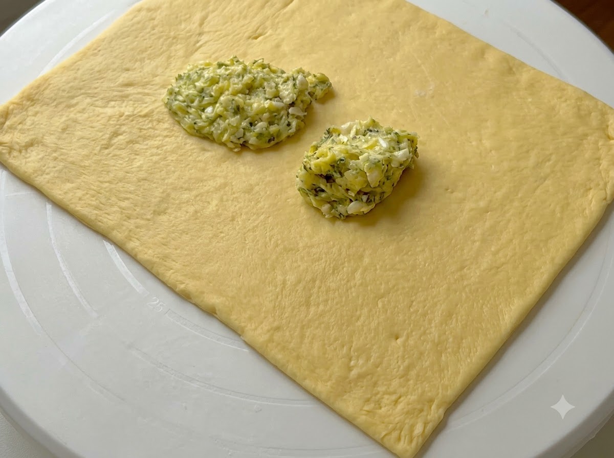 Mucchietti di crema di burro allaglio verde sopra un foglio rettangolare di impasto appiattito.