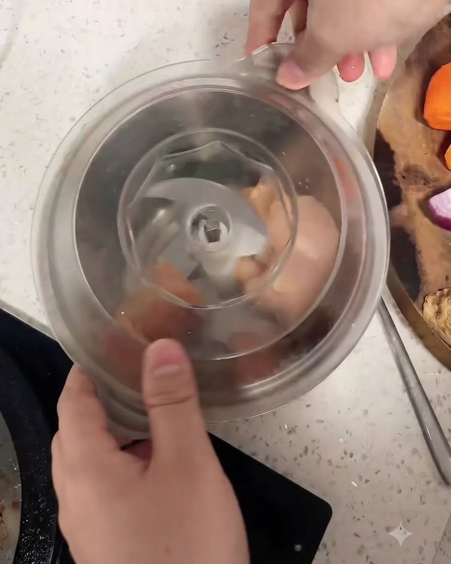 Pezzi di petto di pollo crudo allinterno della ciotola di un robot da cucina attorno alla lama centrale.