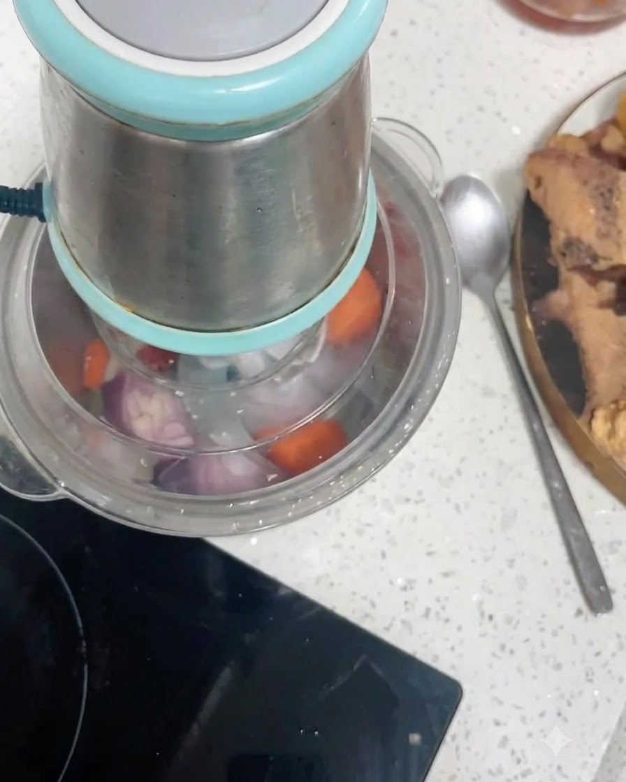 Pezzi di carota e cipolla rossa allinterno del contenitore di un robot da cucina mentre vengono tritati.