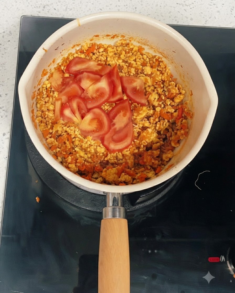 Fette di pomodoro fresco adagiate sopra il composto cotto di pollo e verdure in una padella.