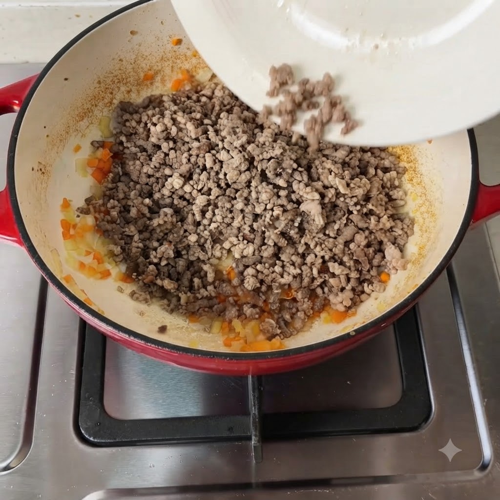 Vari condimenti e pomodori a pezzi aggiunti al composto di carne e verdure.