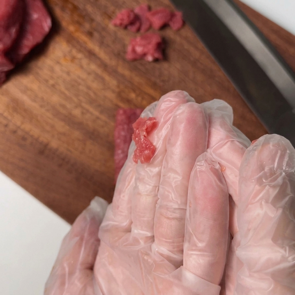 Filetto di manzo affettato mescolato a mano con i condimenti in una ciotola.