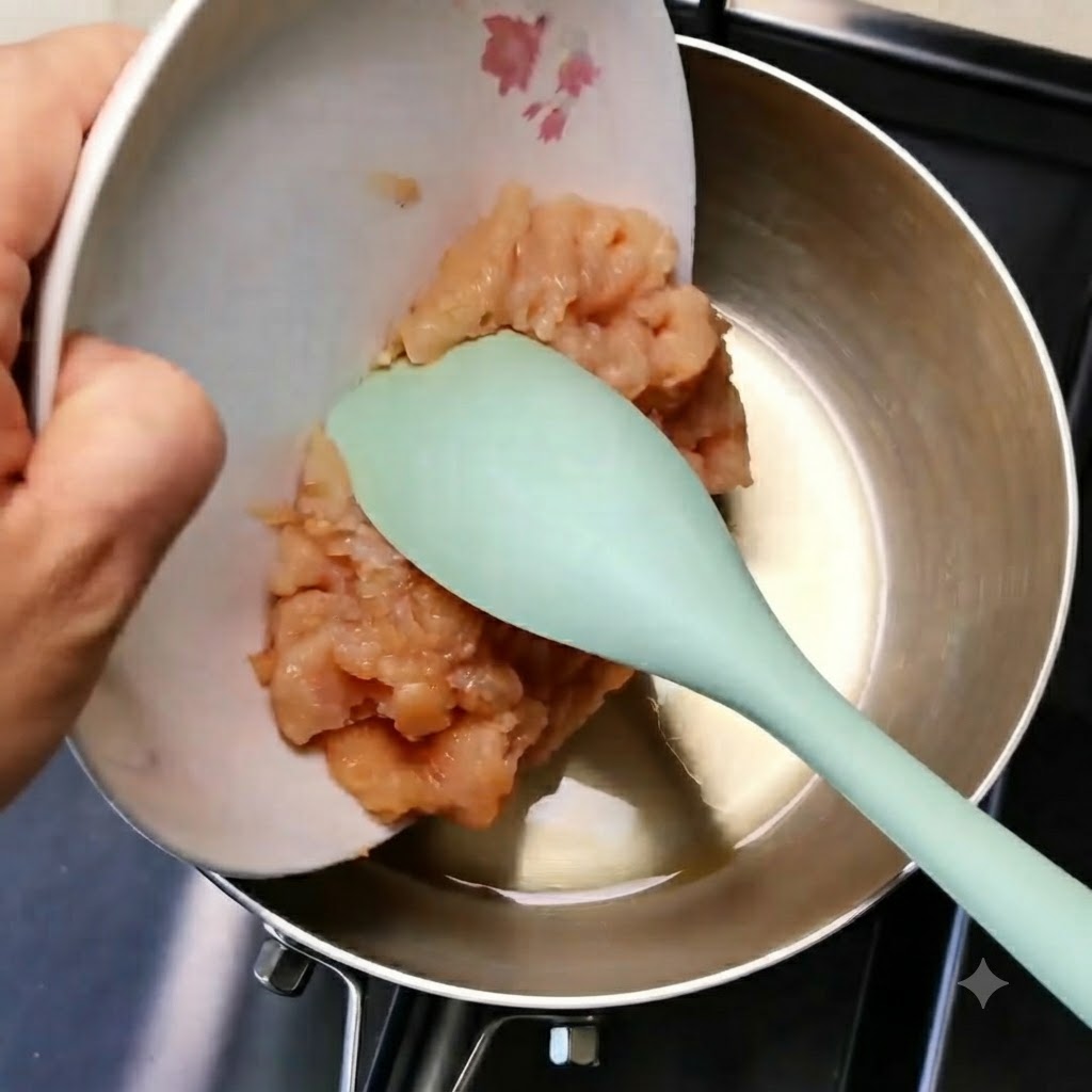 Carne di pollo macinata che scivola da un piatto bianco in una padella di metallo usando una spatola verde.