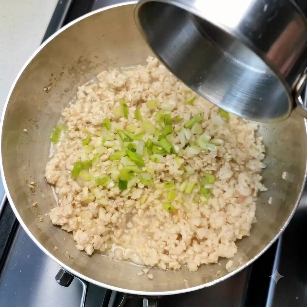 Cipollotti tritati e aglio sparsi sul pollo macinato cotto allinterno di una padella.
