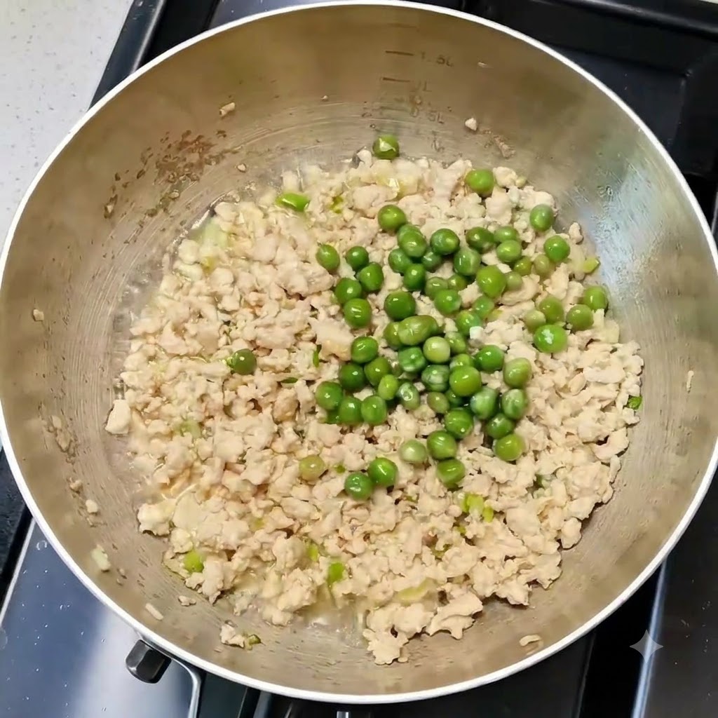Piselli verdi mescolati uniformemente con pollo e aromi in una padella.