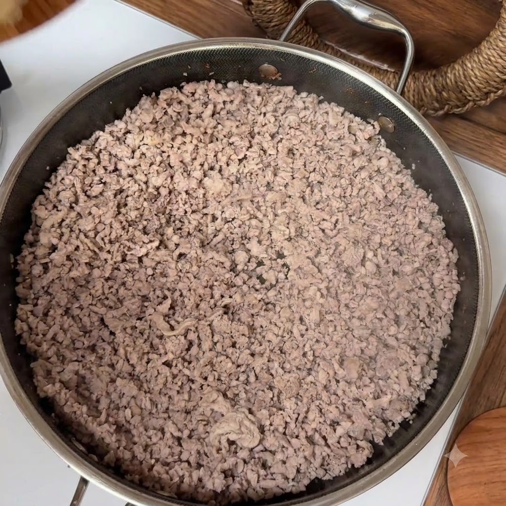 Carne macinata cotta che riempie una padella in acciaio inossidabile durante il processo di rosolatura.