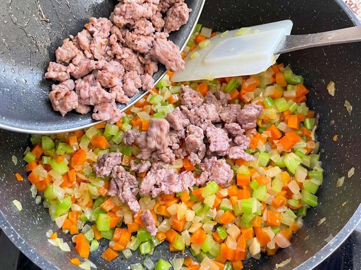Carne di salsiccia cotta versata da una padella nella pentola delle verdure e mescolata.