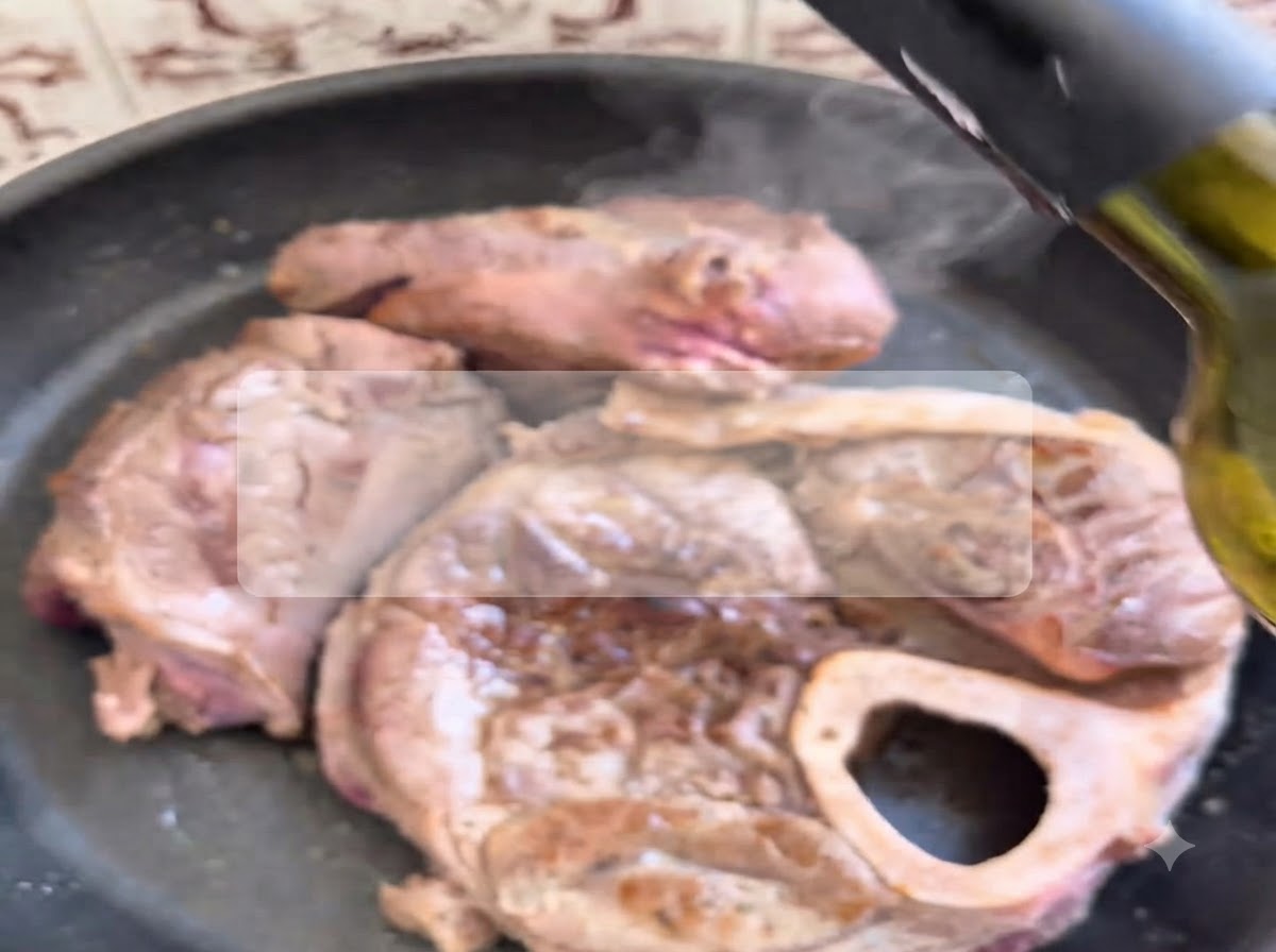 Vino rosso versato da una bottiglia su tagli di manzo rosolati che sfrigolano in una padella calda.