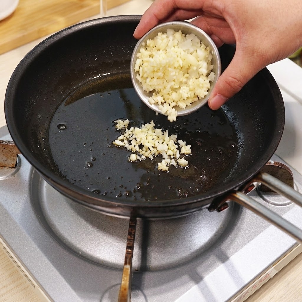 Aglio tritato e cipolla versati da una ciotolina in una padella calda con olio.