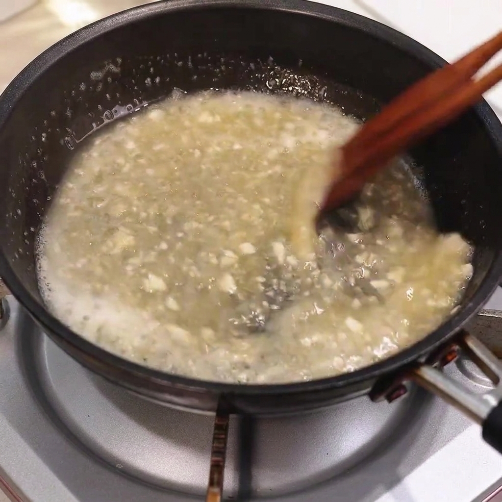Burro che si scioglie in una salsa in padella che sobbolle, mentre viene mescolato con bacchette di legno.