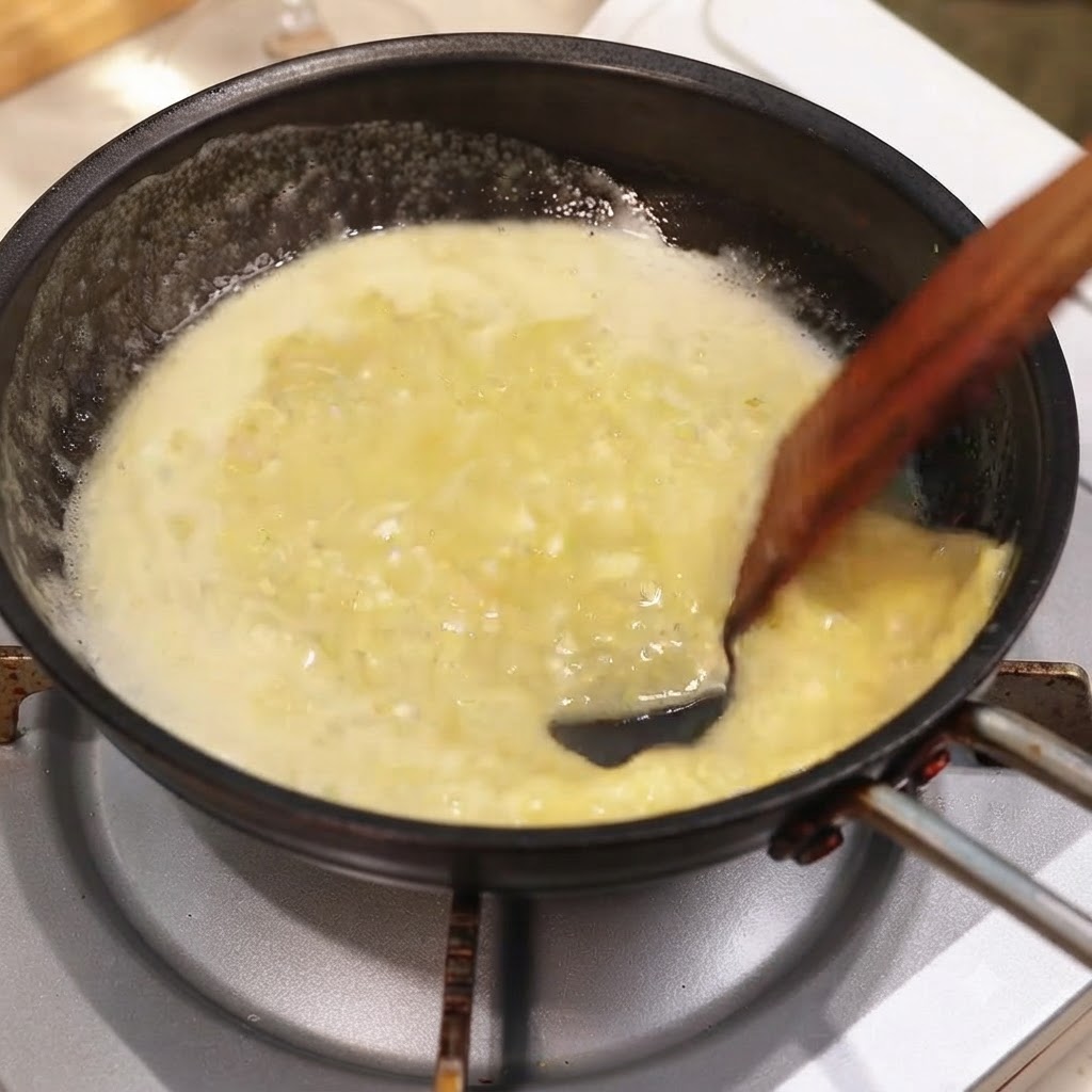 Una padella di ricca salsa al burro, limone e aglio mescolata con erbe tritate usando una spatola di legno.