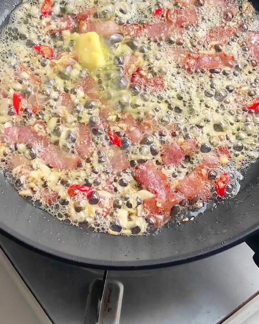 Noodles di pasta cotti aggiunti a una padella piena di pancetta sfrigolante, burro fuso, aglio tritato e peperoncini rossi a fettine.