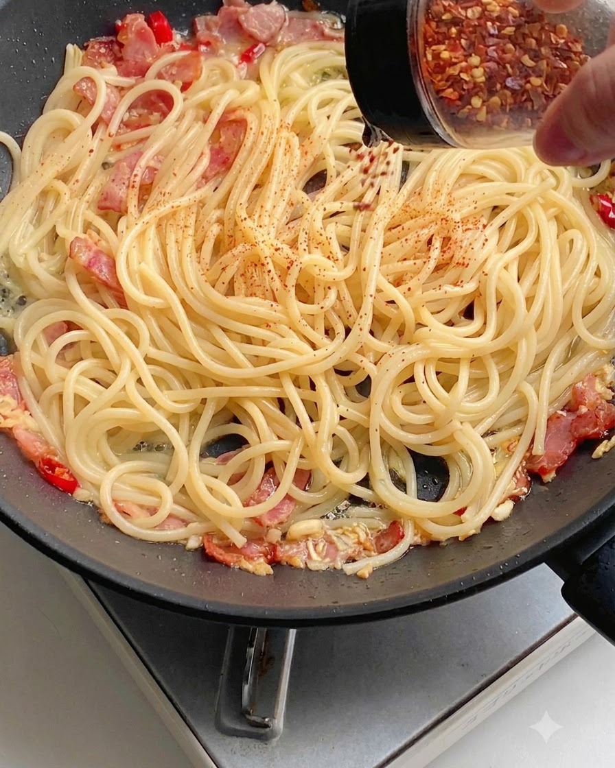 Peperoncino rosso in polvere cosparso uniformemente sugli spaghetti in padella.