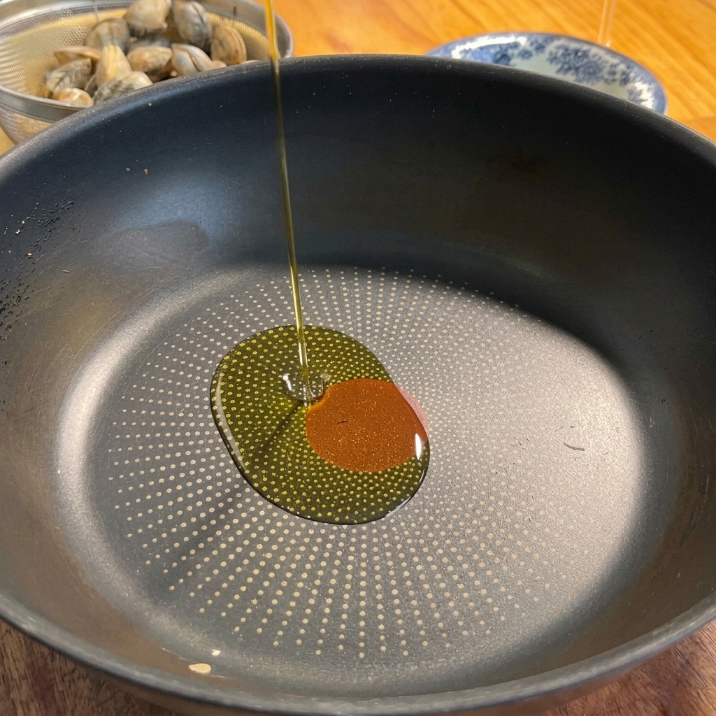 Olio doliva versato in una padella insieme ad aglio e peperoncino.