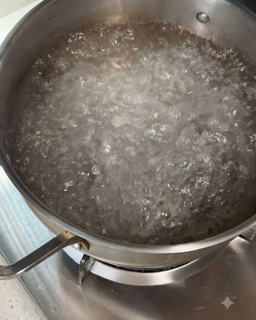 Pasta secca che viene mescolata in una pentola di acqua bollente usando degli utensili.