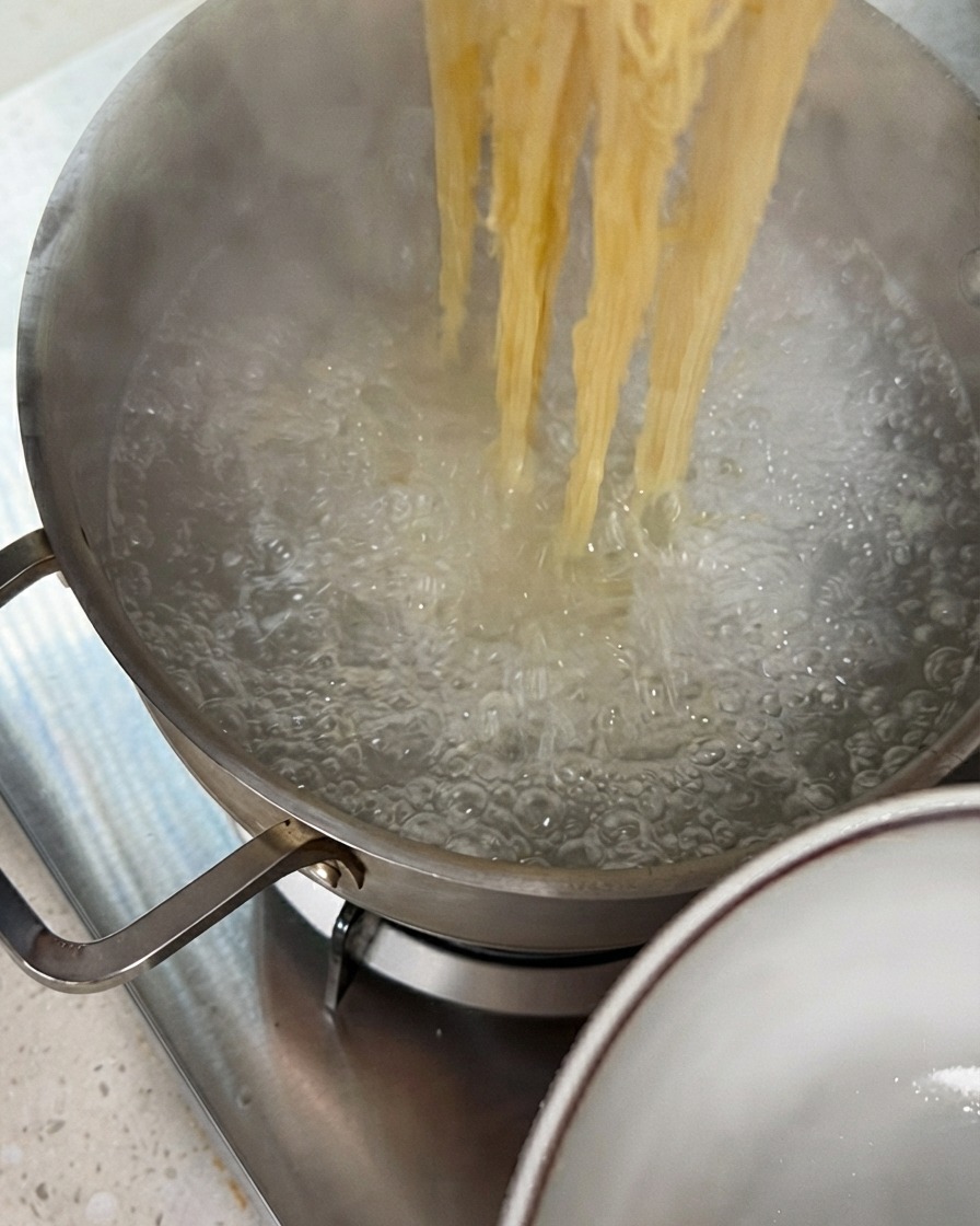 Pinze che sollevano fili di pasta cotta da una pentola dacqua bollente.