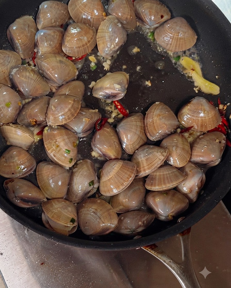 Vino bianco versato da una bottiglia in una padella sfrigolante riempita di vongole, aglio e peperoncini.