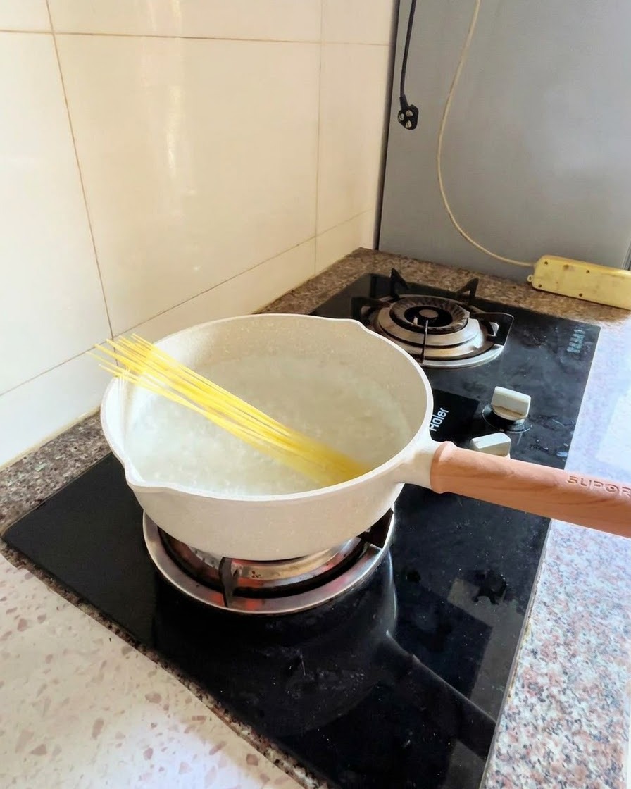 Spaghetti crudi immersi diagonalmente in una pentola di acqua bollente sul fuoco.