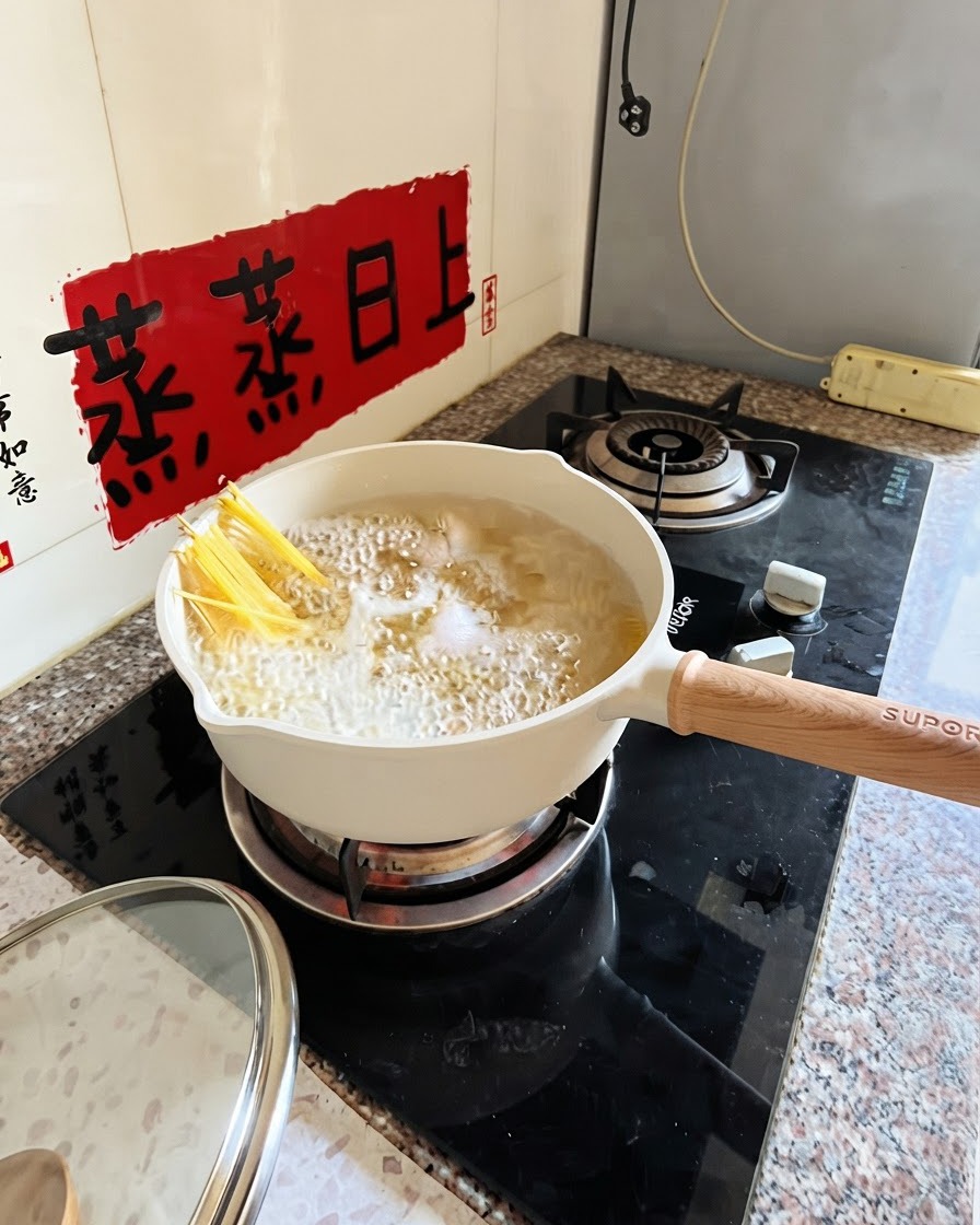 Spaghetti in ebollizione in una pentola bianca con pinze che li immergono parzialmente.
