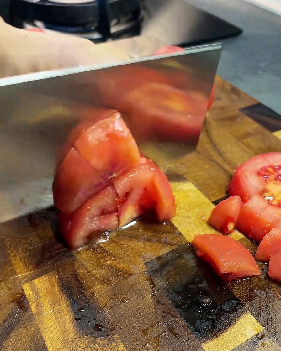 Pomodori pelati affettati a piccoli pezzi con una mannaia su un tagliere di legno.