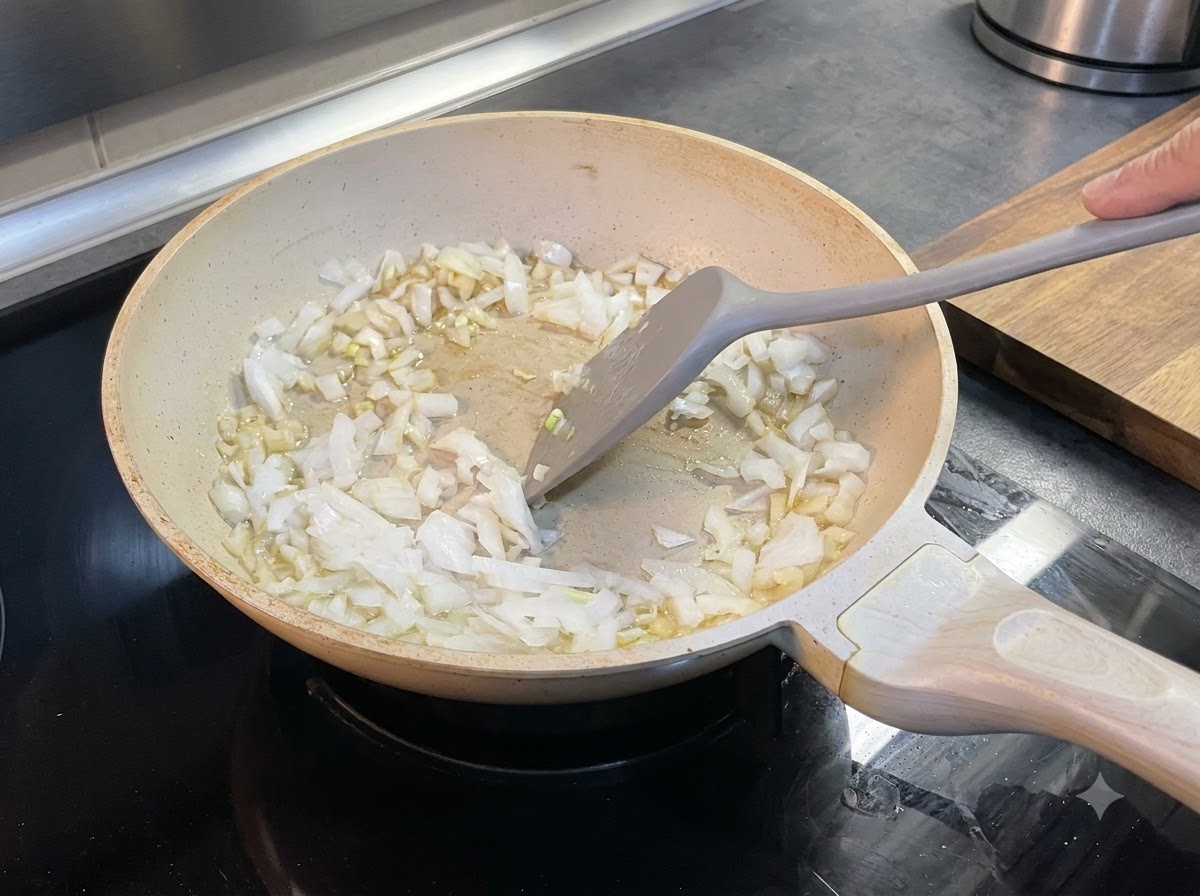Cipolle tritate mescolate nel burro fuso dentro una padella usando una spatola.