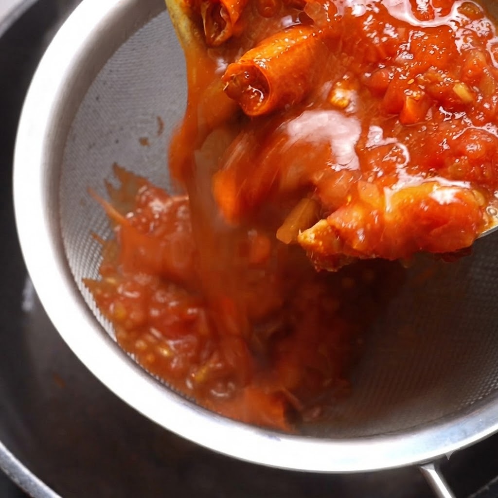 Salsa di pomodoro cotta versata attraverso un setaccio di metallo con una spatola che preme il contenuto.